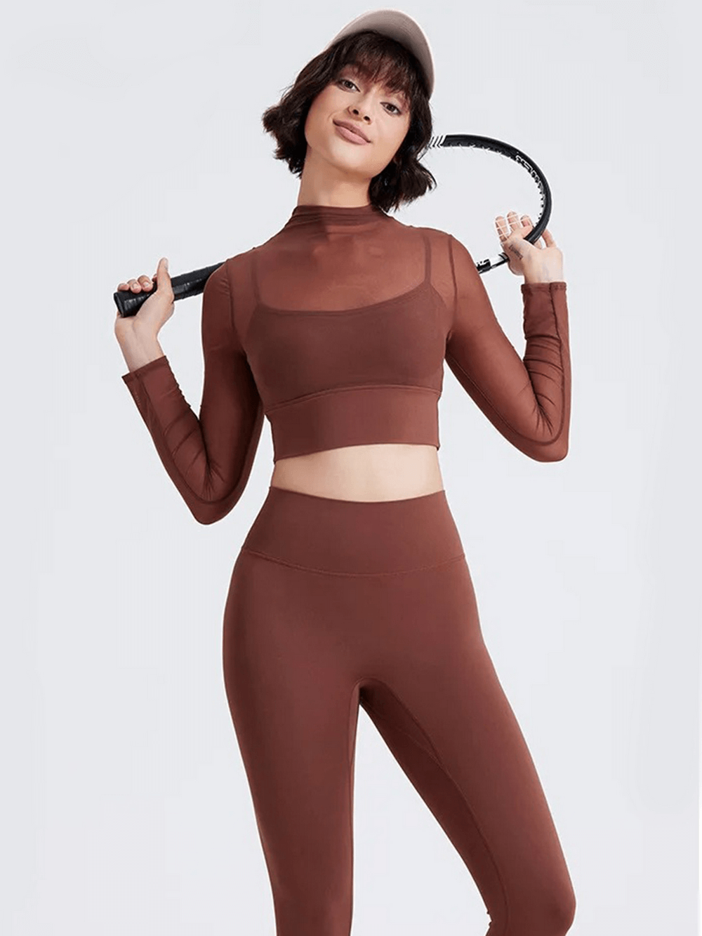 Woman in brown mesh crop top with long sleeves holding tennis racket, showcasing sporty and stylish activewear.